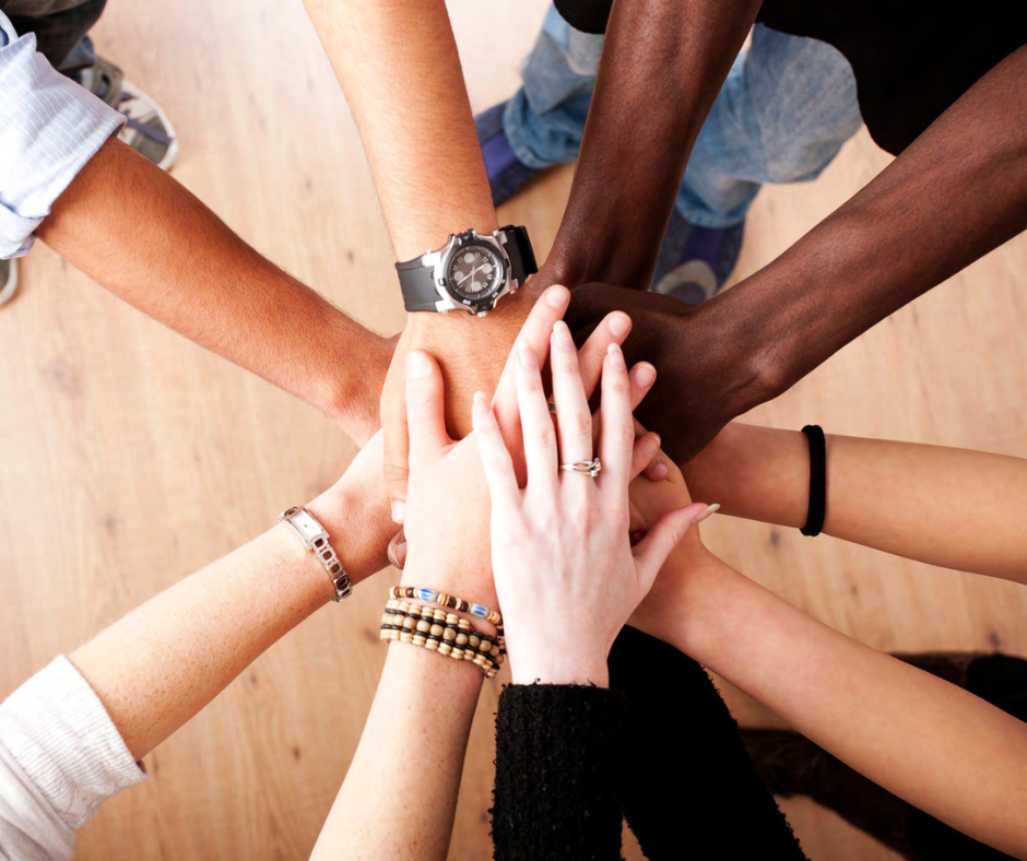 multiple people's arms coming together with hands on top of one another