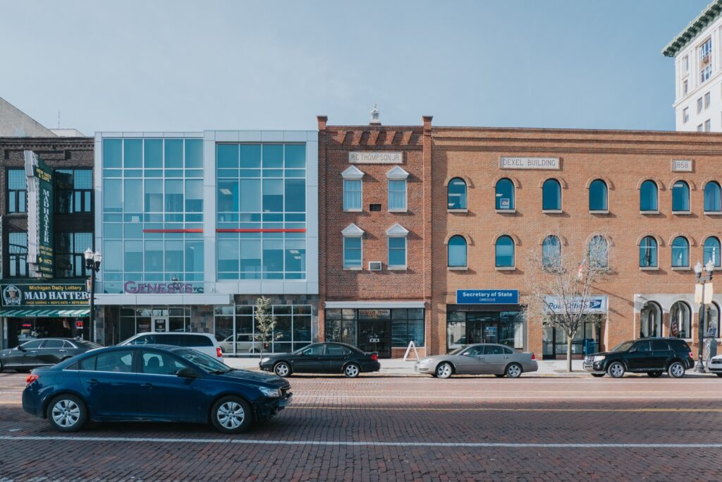 Picture showing a block of buildings downtown Flint, including the Mad Hatter, Genesys Health Care, the USPS, and the Michigan Secretary of State.