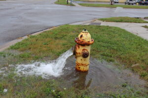 A yellow fire hydrant, opened and draining water onto the right-of-way next the street