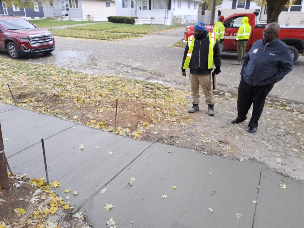 Clyde Edwards and City employees stand next to and look at a freshly poured section of sidewalk.