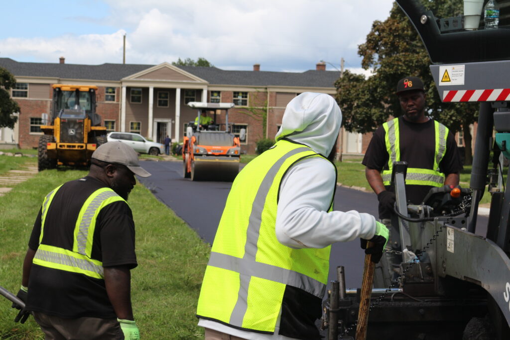 A City crew paving a neighborhood street, steamroller in the background