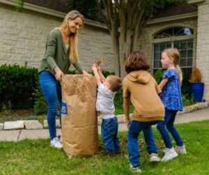 A mother and three children filling a lawn bag with leaves.