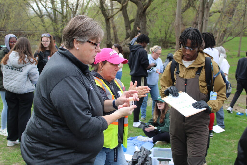 Foreground: Tiffany Minder, Environmental Compliance Supervisor for the Flint Water Treatment Plant (Left), and Tracey Smith, MS4 coordinator for the City of Flint, show Flint Southwestern Academy Students how to collect and test water samples.