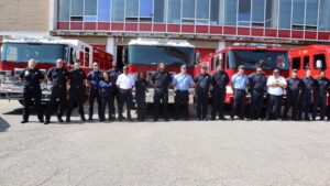 Members of the Flint Fire Dept. stand in the in front of fire trucks with Flint Fire Station #1 behind them.