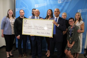 Mayor Sheldon Neeley standing with Dr. Jawad Shah, CEO Insight Health System, and Insight staff with a check for $500,000 from the City of Flint.