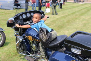 A small boy sitting on a Flint Police Department motorcycle, looking back over his shoulder and smiling at the camera