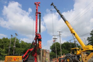 A tall crane holding an equally tall pile driver inserting new underground pilings at the Third Avenue pump station. 