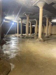 Inside view of the Cedar Street Reservoir emptied of water showing large support columns and lit by a work light. 