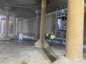 Workers inside the Cedar Street Reservoir emptied of water, some standing on scaffolding to perform repairs to the sides and top of the underground structure.
