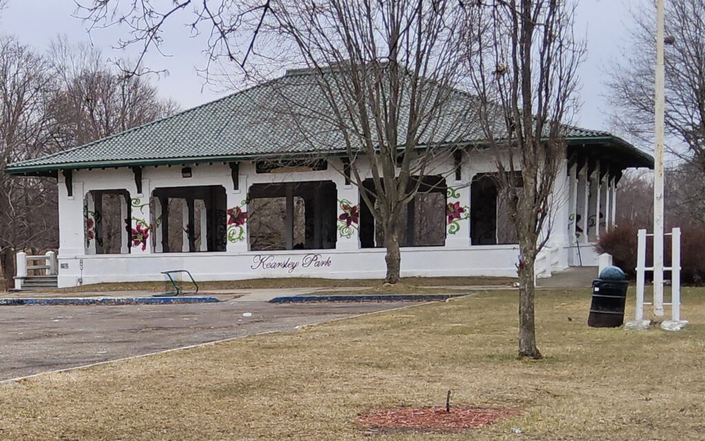 A picture of the Kearsley Park pavilion showing newly painted images of roses on the columns and the name in cursive on the lower wall. Picture was taken sometime in the late fall or early spring.