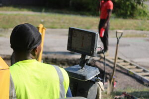 Looking over a machine operator's shoulder at a monitor used to align the bore used to replace service lines. Another worker stands in the background.